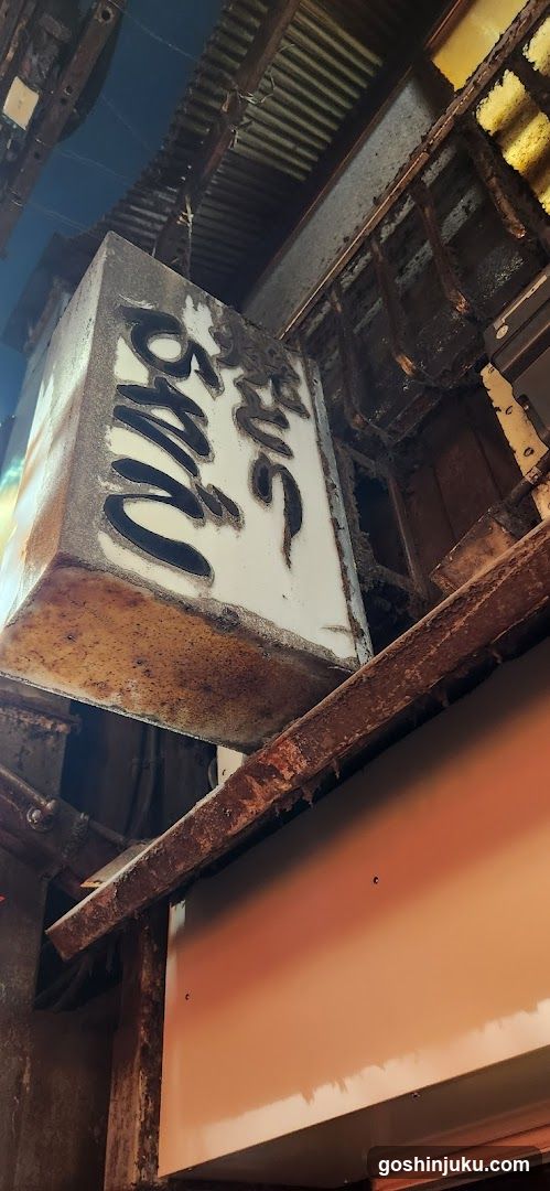 A weathered, rectangular sign with bold black lettering mounted on a dilapidated wooden structure above an entrance. The building facade shows signs of decay and age.