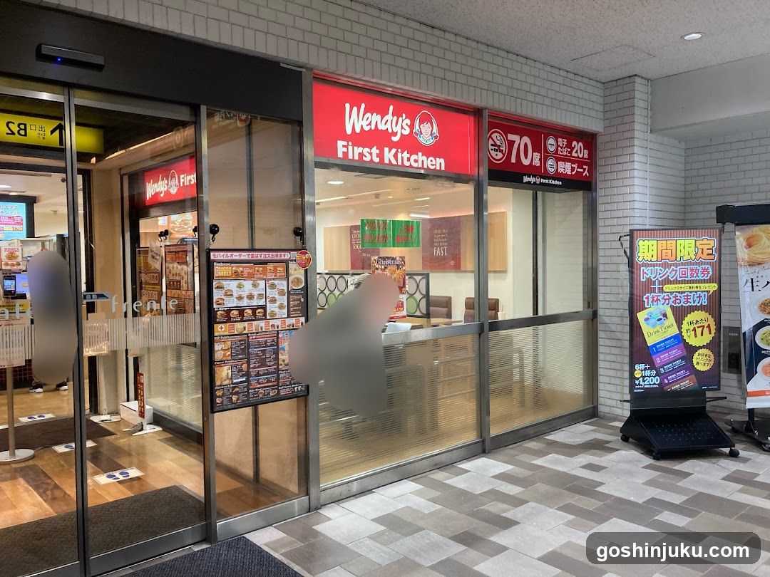 Exterior view of Wendy's First Kitchen with visible signage, glass entrance doors, and promotional posters inside and outside the store.