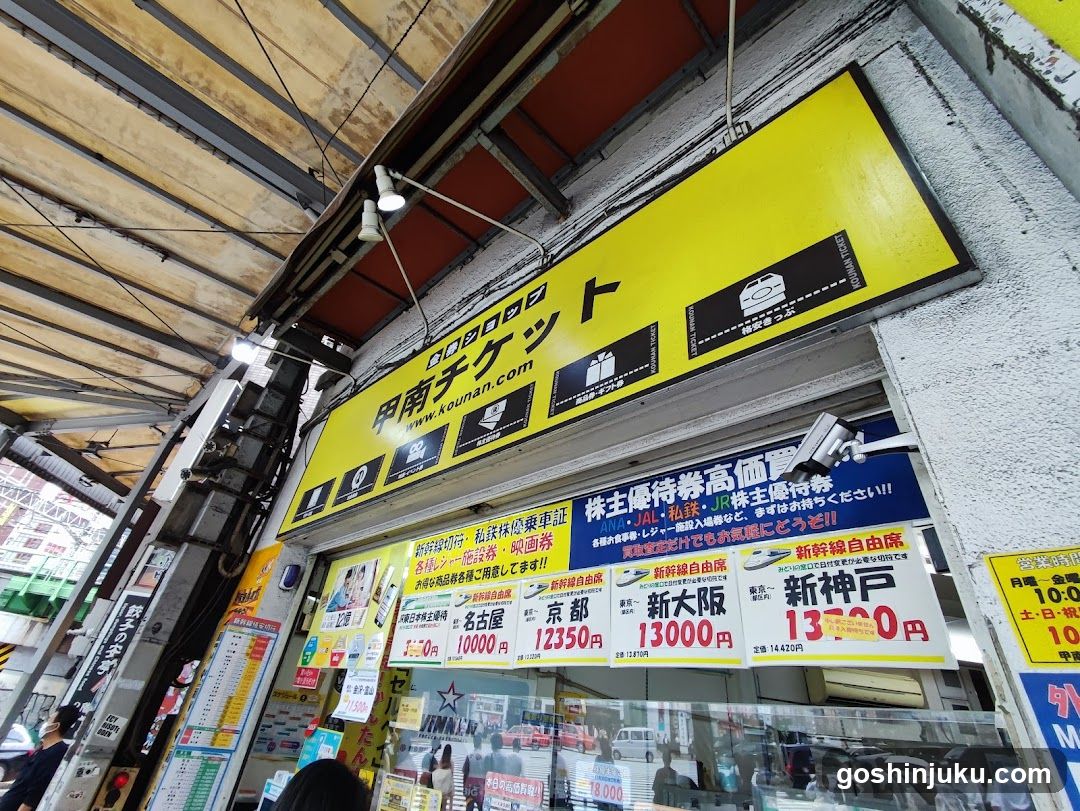 A shop front with a yellow signboard displaying ticket information and prices, including train tickets to various destinations like Kyoto, Osaka, and Shinkansen.