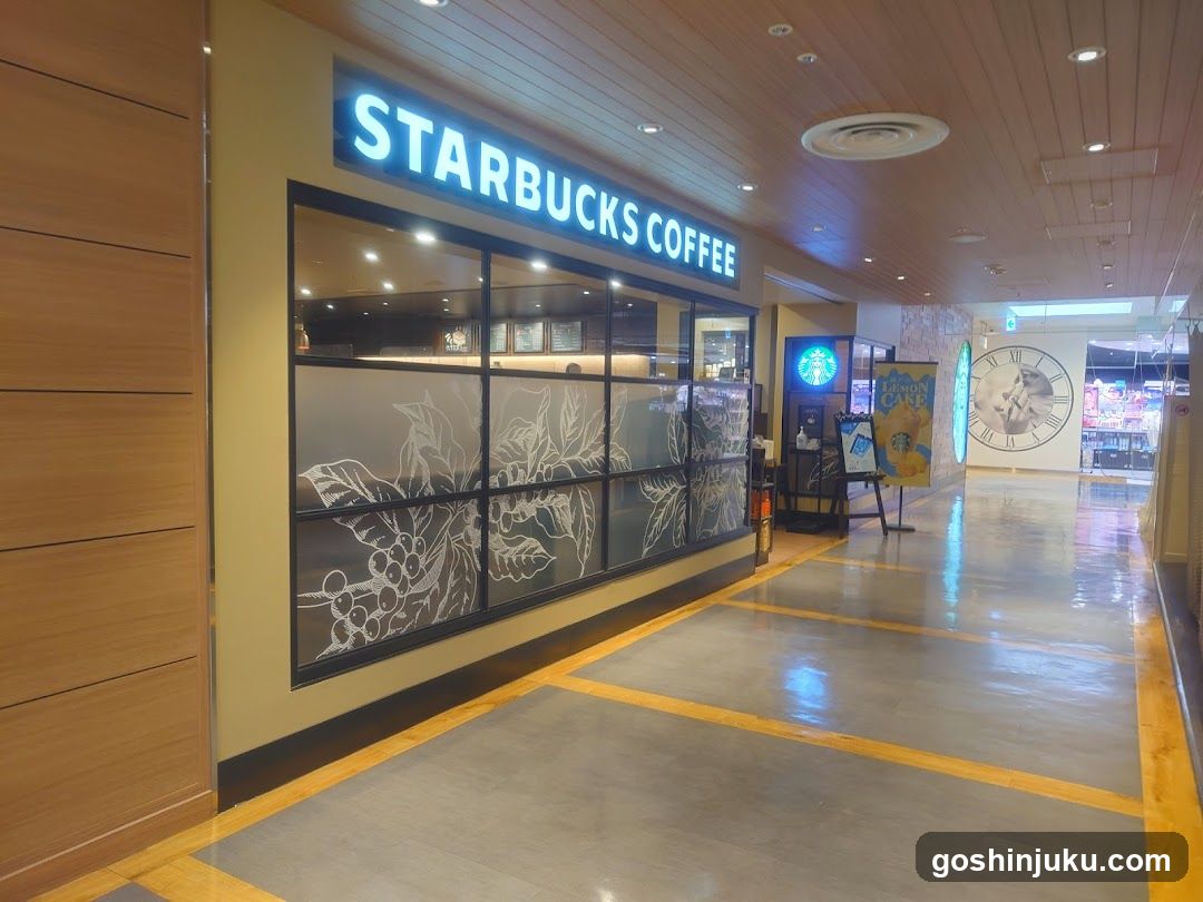 A Starbucks Coffee storefront with illuminated signage above frosted glass windows featuring coffee plant etchings. A promotional standee and a large clock are visible in the background hallway.