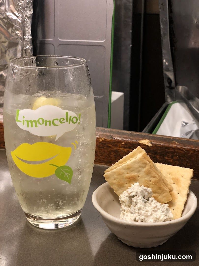 A glass of sparkling lemonade with a lemon slice, featuring the word 'Limoncello' in green text above yellow lips graphic. Next to it is a small bowl containing crackers and a creamy dip.