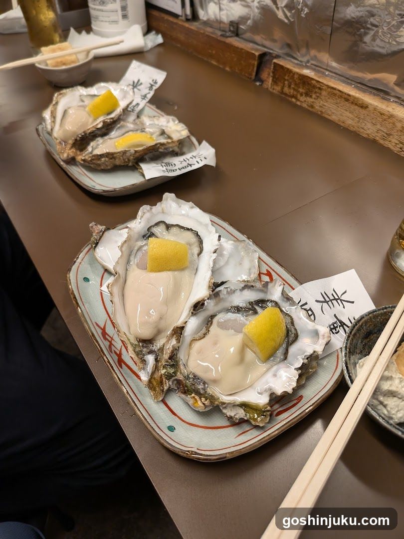 A close-up of two plates of raw oysters, each garnished with a wedge of lemon. The plates are placed on a wooden table in what appears to be a restaurant setting. Chopsticks and other dining utensils are visible nearby.