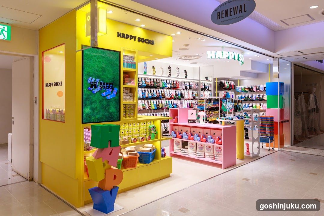 A brightly colored storefront with yellow and pink displays, featuring shelves of socks and other merchandise. The sign 'HAPPY SOCKS' is visible above the entrance.