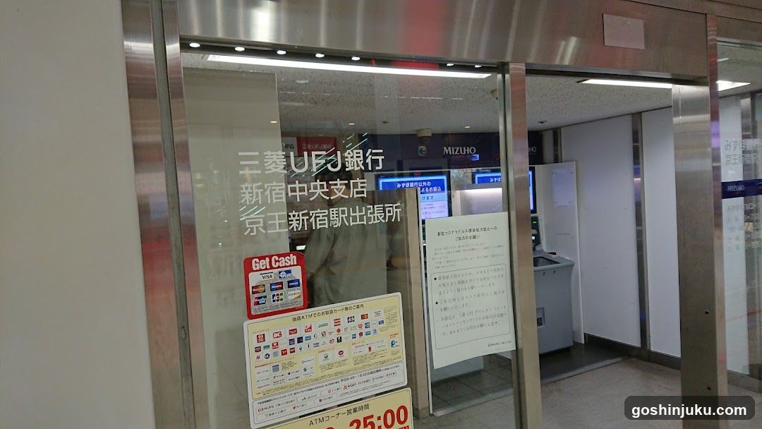 Entrance to Saito UFJ Bank Shinjuku Central Branch, located at Keio Shinjuku Station Exit 5. Visible signage includes 'MIZHO' and ATM hours (24:00). Posters display card logos and ATM usage instructions.