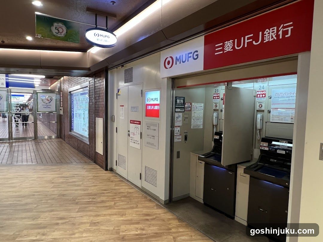 Interior view of a MUFG (Mitsubishi UFJ Financial Group) bank branch showing self-service ATMs and signage. Visible elements include the red '三菱UFJ銀行' sign above the entrance, circular 'MUFG' logo on ceiling, informational posters near doors, and two open ATM machines with blue lighting underneath. The floor is light wood laminate; brick wall section to left leads toward glass exit doors. No menu boards or food items present.