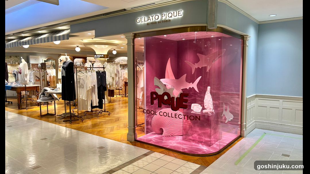 Store entrance with pink glass display featuring shark silhouettes and 'PIQUE COOL COLLECTION' branding. Interior shows clothing racks, mannequins, and wooden flooring under warm lighting.