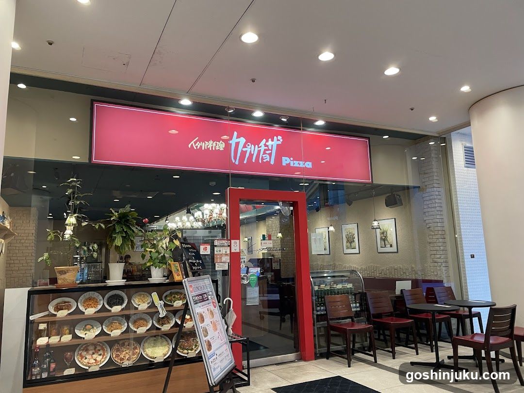 A storefront with a red sign displaying 'Pizza' and Chinese characters, featuring glass windows, potted plants inside, and a display case showing various food items.