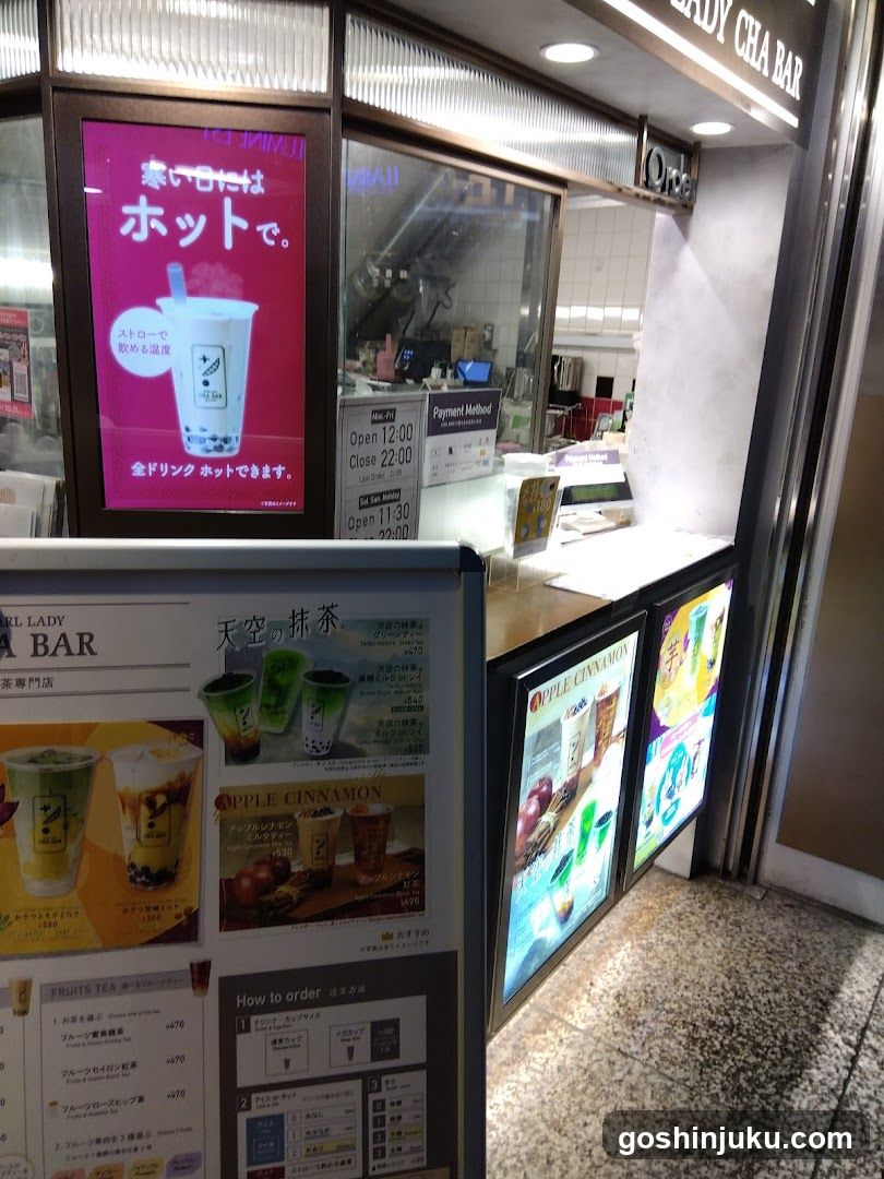 A photo of the exterior entrance to a Lady Cha Bar shop, featuring illuminated signage and menu boards displaying drinks like Apple Cinnamon and Sky Tea.