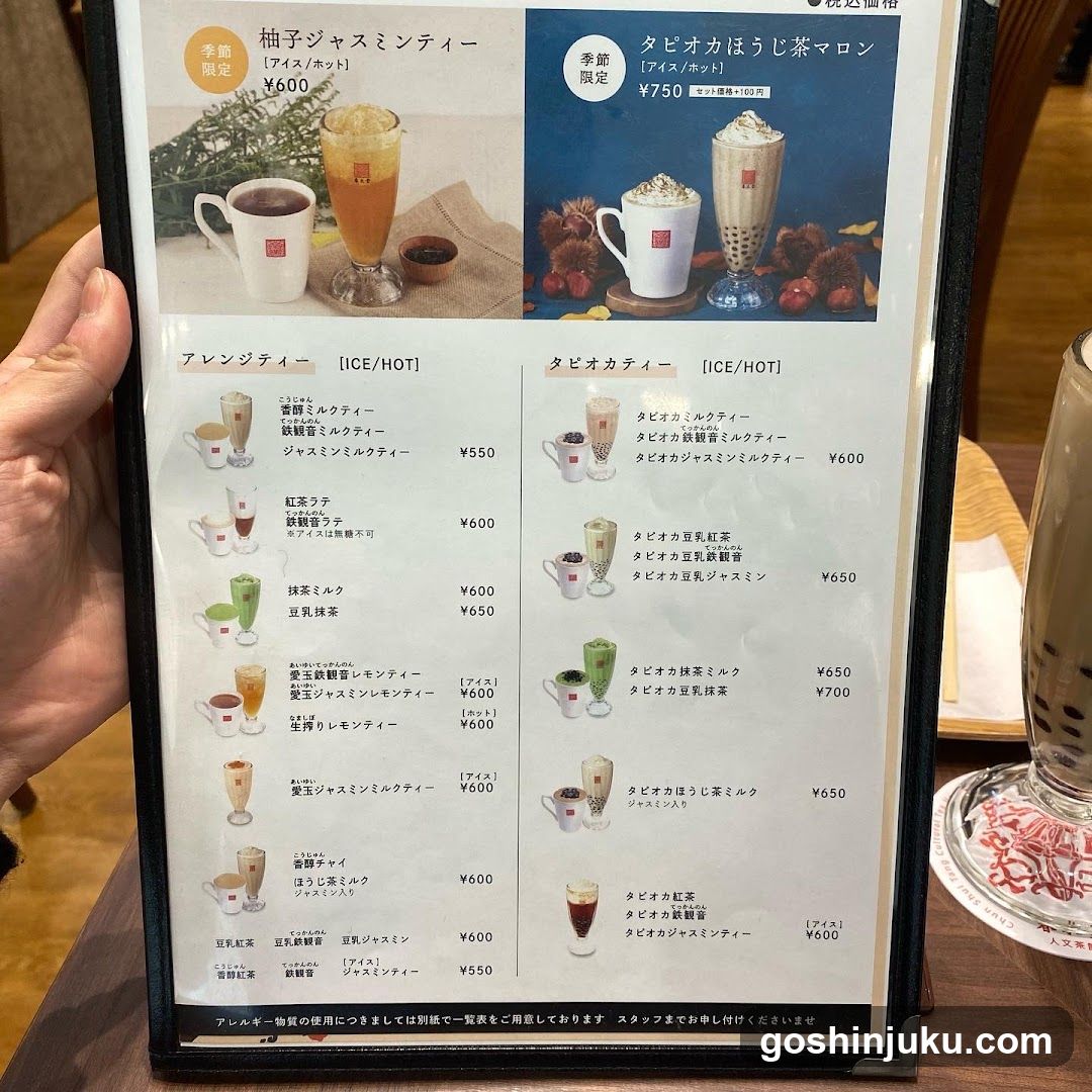 A close-up of a printed menu board held by hand, featuring Japanese and English text with images of drinks like lemonade, bubble tea, and milkshakes.