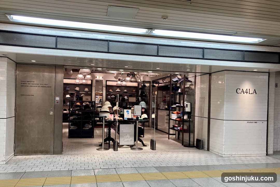 A storefront with a large glass entrance, displaying various hats on shelves and mannequins inside. The exterior wall features the text 'CA4LA' in bold letters. Inside, there are multiple racks of hats, some hanging from the ceiling, and promotional signs near the entrance.