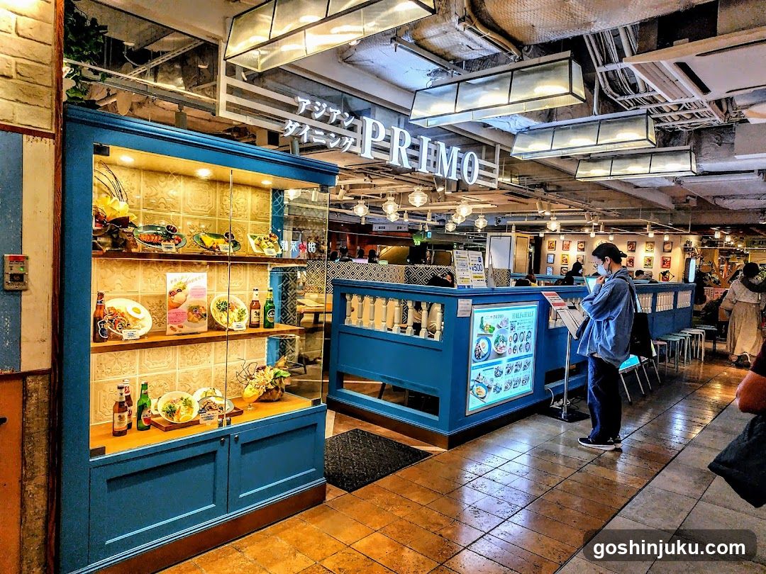 Interior view of a restaurant with blue display cabinets showcasing food items, menu boards on the counter, and customers browsing.