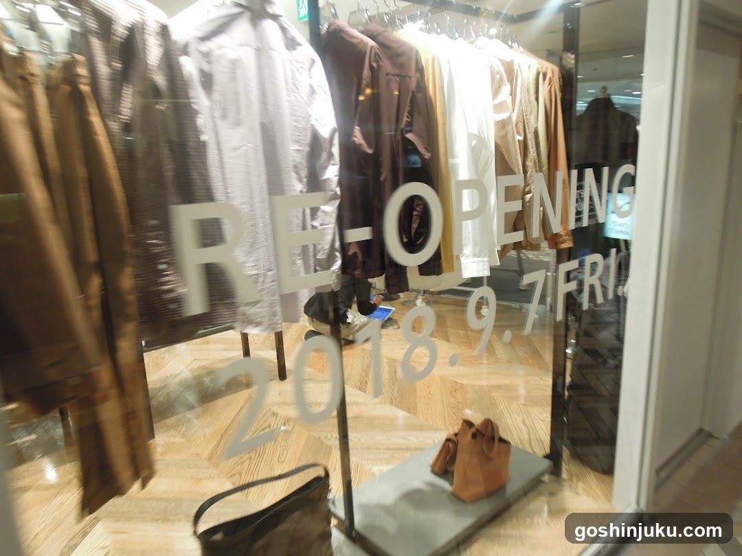 A glass storefront window displays hanging clothing items in neutral tones, with 'RE-OPENING' and the date '2018.9.7 FRI' etched on the glass.