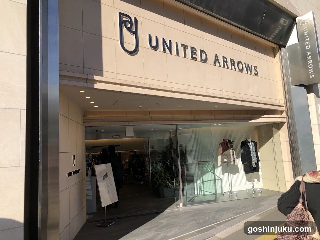 Exterior view of a United Arrows store entrance with glass doors and mannequins displaying clothing in the window.