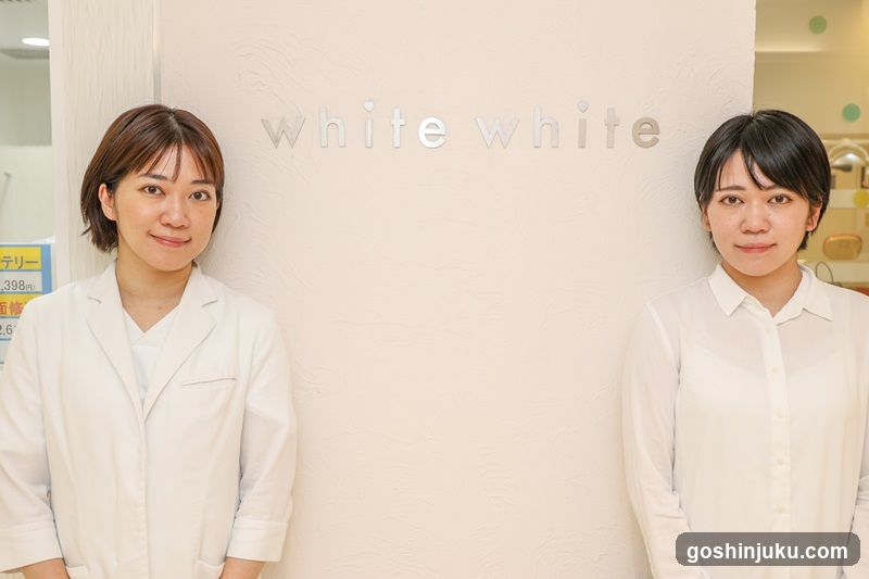 Two women in white standing in front of a wall with 'white white' sign