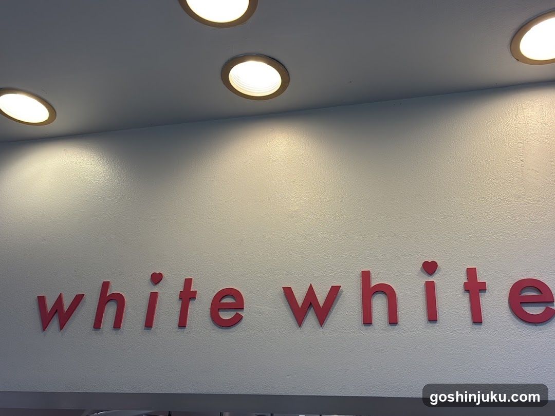 A close-up view of a white wall with red lettering spelling 'white white', featuring small heart symbols above the 'i's in each word. The scene includes recessed ceiling lights illuminating the signage, suggesting an interior or storefront entrance.